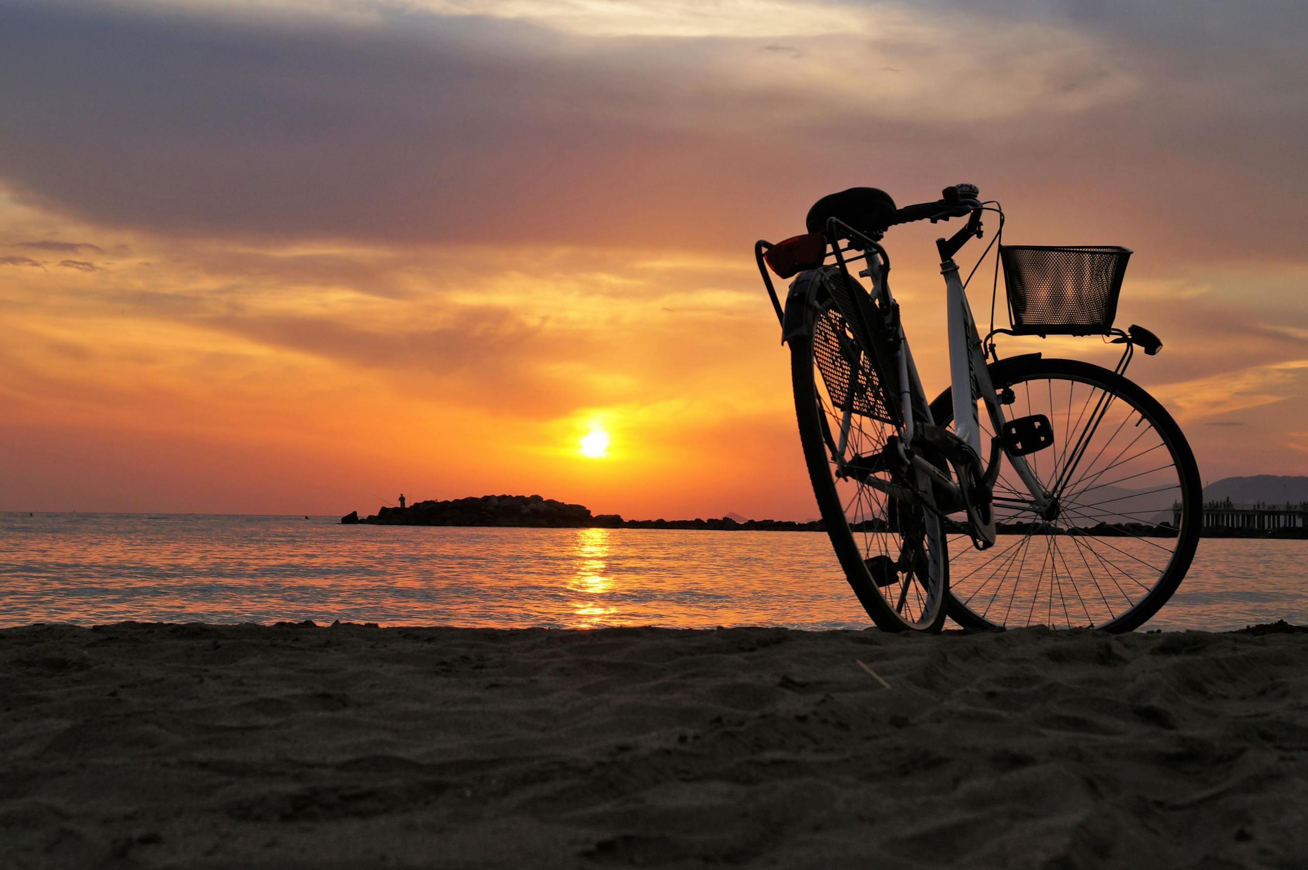 Silhouette of a bicycle on a sandy beach during a vibrant sunset over the ocean. Representing about révelo pb