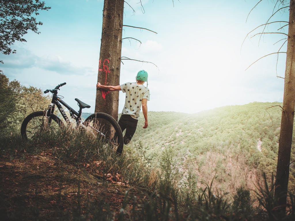 Teenager with bike on a mountaintop, enjoying the scenic landscape and summer freedom.